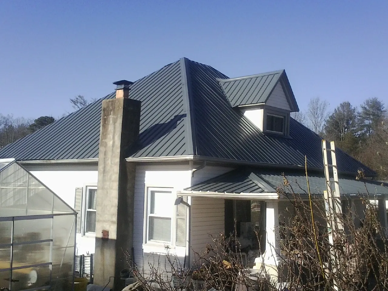 Dark blue standing seam metal roof on a white farmhouse with dormer — Slate & Tile Roof Repair by Roofing Brothers in Rockville Centre
