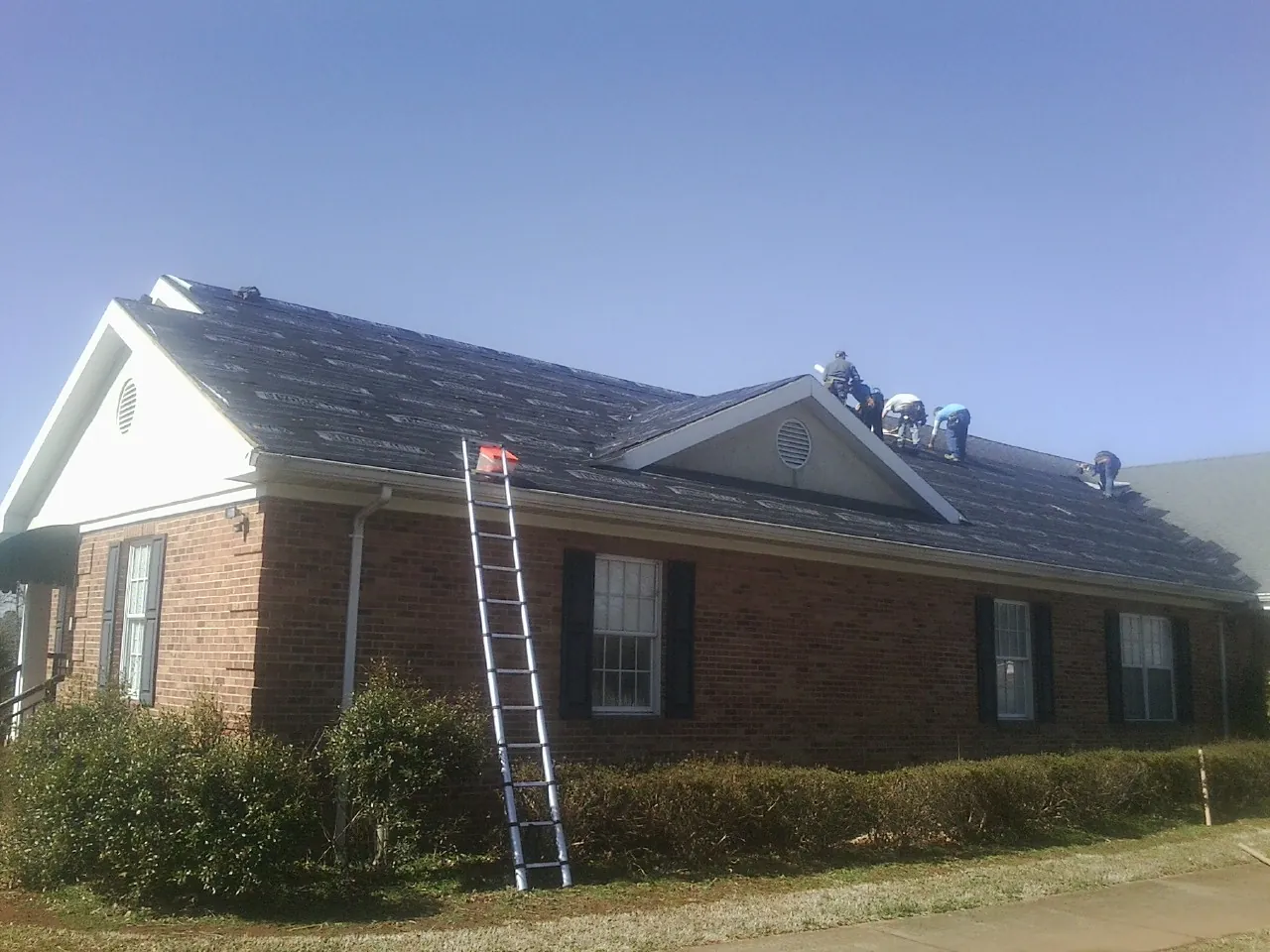 Crew tearing shingles off a brick ranch roof with a ladder set — Emergency Roof Repair work by our crew in Rockville Centre