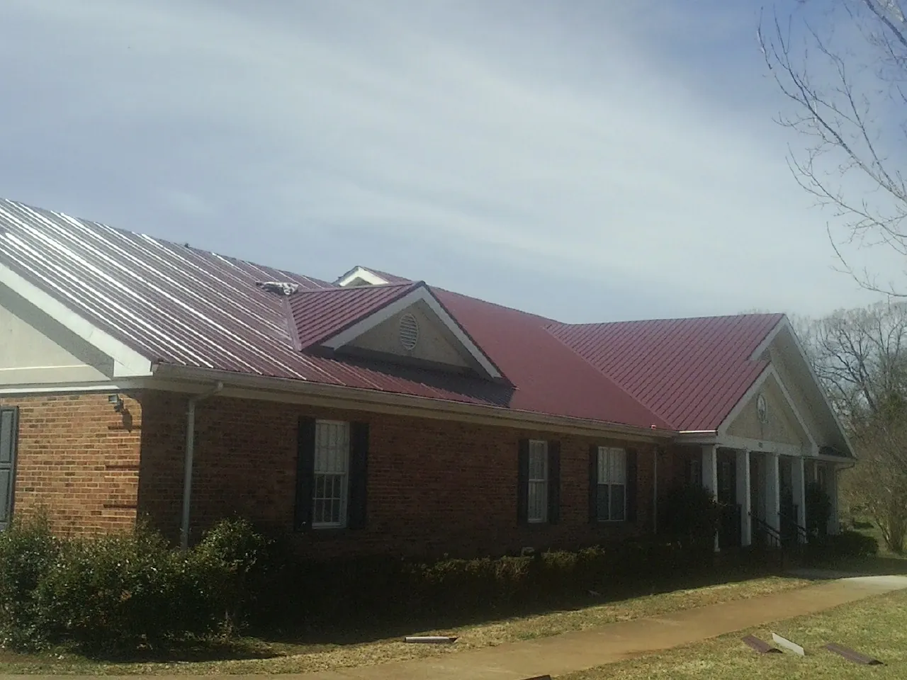 Red metal roof with gabled entries on a long brick building, from a Hail Damage Roof Repair job in Rockville Centre