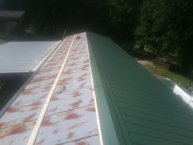 Old rusted panels beside newly installed green metal roofing — Wind Damage Roof Repair by Roofing Brothers in Rockville Centre