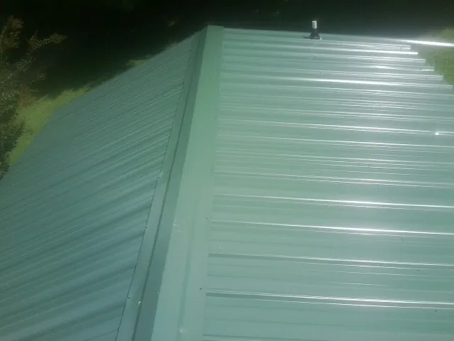 New green metal panels meeting at the ridge of a roof — Flat Roof Repair work by our crew in Rockville Centre