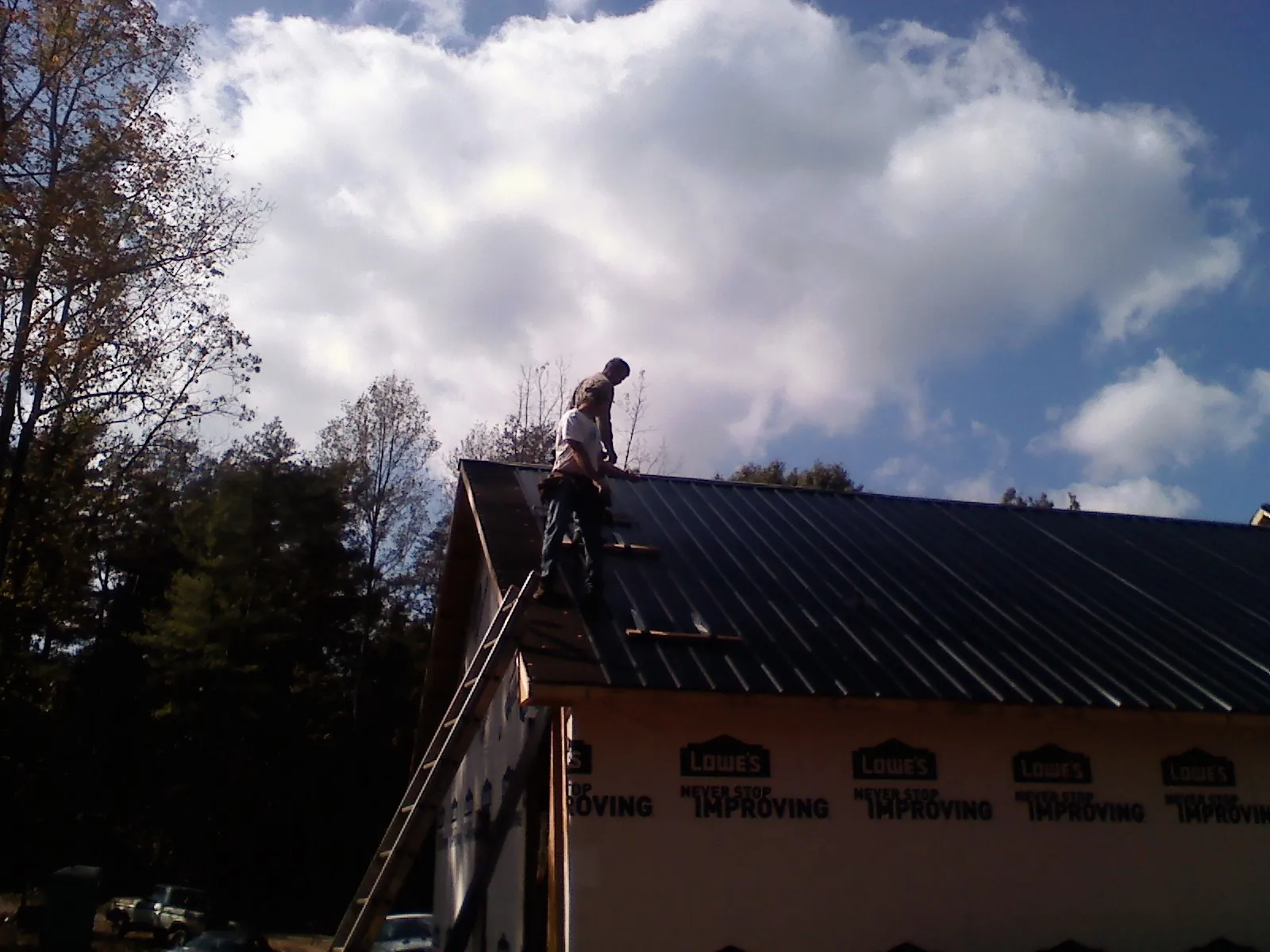 Roofer fastening dark metal panels high against a cloudy sky, from a Roof Inspection job in Rockville Centre