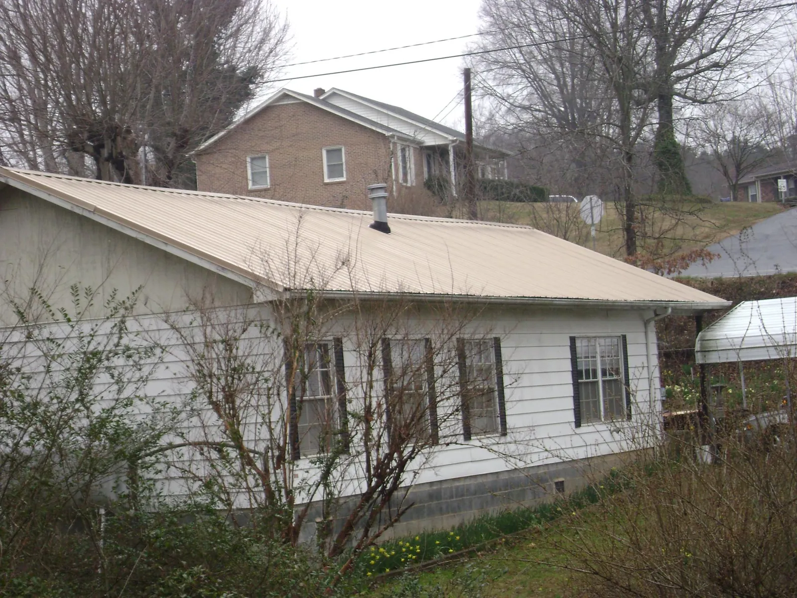 Tan metal roof on a white sided house set into a hillside — Commercial Roofing by Roofing Brothers in Rockville Centre